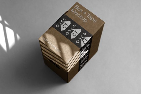 Realistic cardboard box mockup with black tape design on a shadowed surface for packaging and branding presentations.